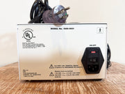 UL certified KMI flow meter pump with a white metal casing, black power cord, and black power outlet on the front, displayed on a wooden surface against a light background.