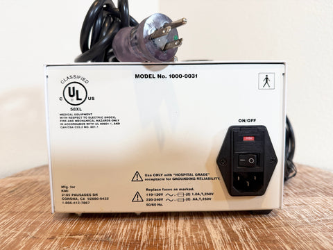 UL certified KMI flow meter pump with a white metal casing, black power cord, and black power outlet on the front, displayed on a wooden surface against a light background.
