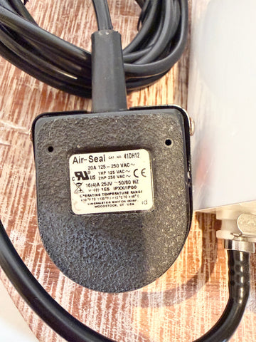 A close-up of a black industrial air seal connector with a textured housing and a white specification label, connected to a black cable on a wood-grain surface.