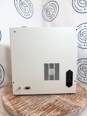 Back view of a white electronic device on a wooden surface with branded boxes in the background.