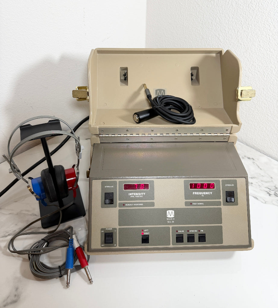 An open beige Maico MA39 Portable Diagnostic Audiometer device with a control panel, digital readouts, attached cables, and a black headset on a white surface against a white wall.