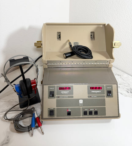 An open beige Maico MA39 Portable Diagnostic Audiometer device with a control panel, digital readouts, attached cables, and a black headset on a white surface against a white wall.
