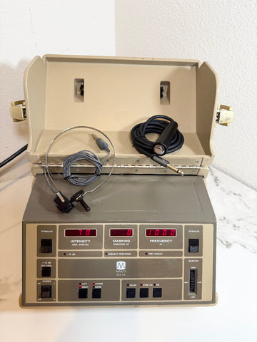 A Maico MA40 Portable Diagnostic Audiometer with an open beige lid, featuring a gray front panel with red digital displays and attached cables, photographed against a white wall and marble-like surface.