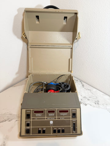 An open beige Maico MA40 Portable Diagnostic Audiometer machine with a control panel on the front, internal wiring, and a red-and-blue bell, photographed on a white marble surface against a white wall.