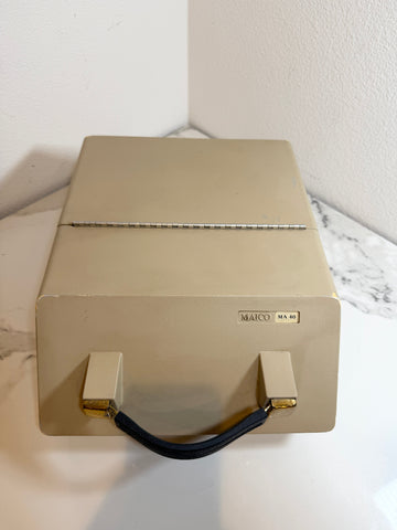 A Maico MA40 audiometer device in a beige box with a black handle and gold accents, sitting on a white marble surface against a white wall.