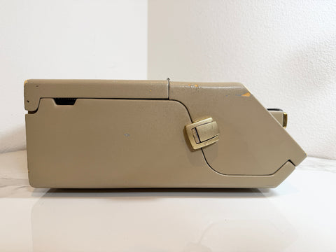 A Maico MA40 Portable Diagnostic Audiometer storage box with a small gold-toned latch, shown from a side profile view on a white surface against a white wall.