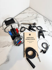 A complete audio interface and headphones kit laid out on a white marble surface, including over-ear headphones, a microphone, cables, an operating instructions booklet, and an audio adapter.