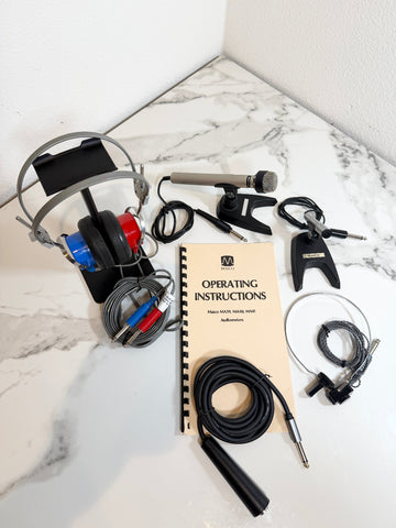 A complete audio interface and headphones kit laid out on a white marble surface, including over-ear headphones, a microphone, cables, an operating instructions booklet, and an audio adapter.