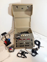 An open beige Maico MA41 Portable Diagnostic Audiometer device with attached cables, a handheld microphone, and a pair of over-ear headphones, arranged on a white marble surface against a white wall.
