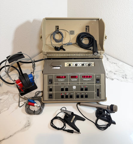 A Maico MA41 Portable Diagnostic Audiometer device with an open beige carrying case, shown on a white marble-like surface against a white wall. The unit has a front control panel with multiple switches, red digital displays, attached black cables, a probe, and other medical accessories arranged around it.