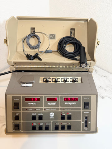 A Maico MA41 Portable Diagnostic Audiometer device with an open beige carrying case, black cables, and a gray control panel with red digital displays, set against a white wall and marble surface.