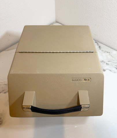 A Maico MA41 Portable Diagnostic Audiometer with a dark blue handle, resting on a white marble-patterned surface against a white wall.