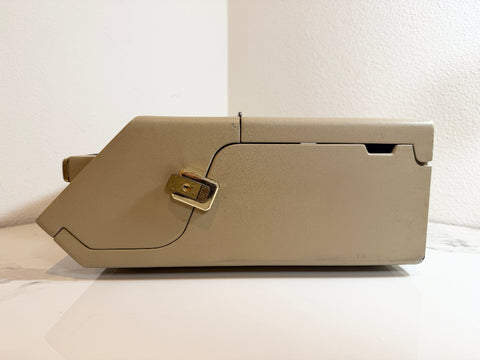 A Maico MA41 Portable Diagnostic Audiometer machine with a gold-colored lock, resting on a white surface against a white wall.