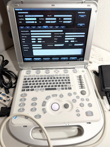 A portable ultrasound machine with a white and gray control panel, open screen showing diagnostic software, and attached cables on a light-colored surface.
