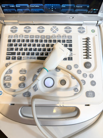 An ultrasound machine with a white control panel, black keyboard, and attached white ultrasound probe with cable, photographed from above.