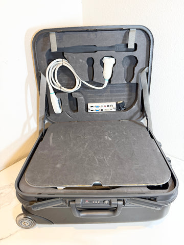 A black hard-shell suitcase opened to reveal a custom-fit Mindray portable ultrasound machine . The case has a padded dark gray cushioned surface, and the interior is organized with a white coiled cable, handheld control unit, and small accessories in foam compartments.