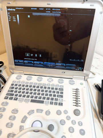 A Mintray portable ultrasound machine with a white plastic housing, gray buttons, and a black screen, shown open on a light-colored surface with cables nearby.
