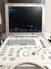 A Mindey ultrasound machine with an open white and gray control panel, showing the screen on and some cables at the side, photographed indoors against a light wall.