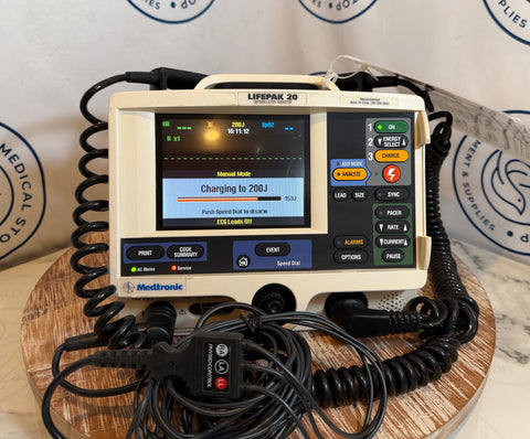 Medtronic Lifepak 20 defibrillator on a wooden surface with cables.