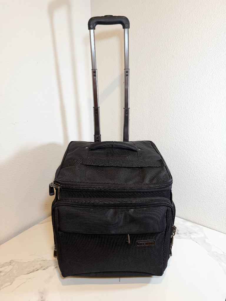 A black soft-sided rolling travel bag with an extended telescoping handle, standing upright on a light marble-like surface against a white wall.