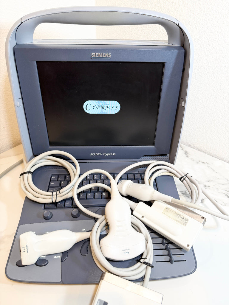 A Siemens Acuson Cypress ultrasound machine with its attached probes, cables, and handpiece arranged in front of the open monitor on a light-colored surface.
