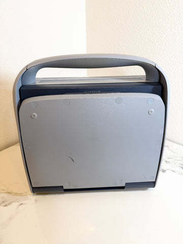 A Siemens Acuson Cypress Portable Ultrasound closed with a built-in handle, shown from the back on a white marble surface against a beige wall.