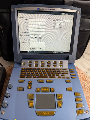 A SonoSite MicroMaxx Portable Ultrasound System shown open and photographed on a tabletop. The device has a slate blue-gray body with gold-colored buttons and a gray screen display showing a patient information form.