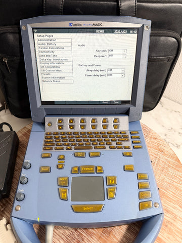 A blue SonoSite MicroMaxx Portable Ultrasound System with a screen, keyboard, and multiple buttons, photographed on a tabletop with a black bag behind it.