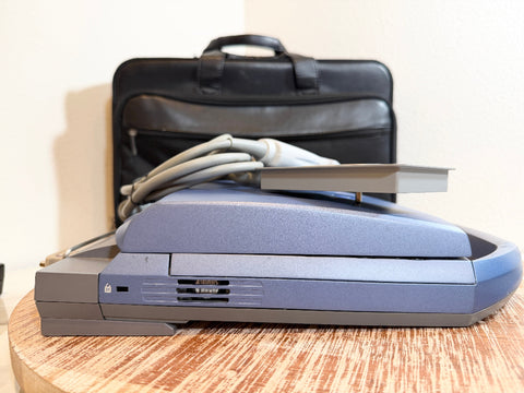 A SonoSite MicroMaxx Portable Ultrasound System sits on a wooden table with its black carrying case and cable behind it against a plain wall.