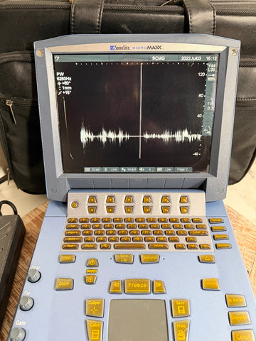 A SonoSite MicroMaxx Portable Ultrasound System with a light blue body, gold-colored buttons, and a black screen displaying a sound wave, set against a dark leather bag background.