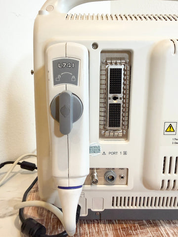 A close-up of Sonoscape ultrasound machine showing the side and back details, including a hand-held probe with a gray control dial, port 1 connector, and warning labels on a beige surface.