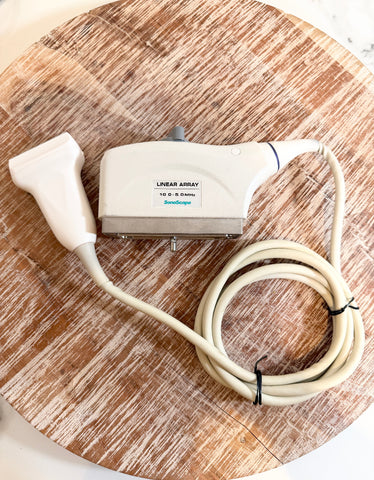 A Sonoscape ultrasound machine linear array probe with a coiled cable, resting on a round wooden cutting board.