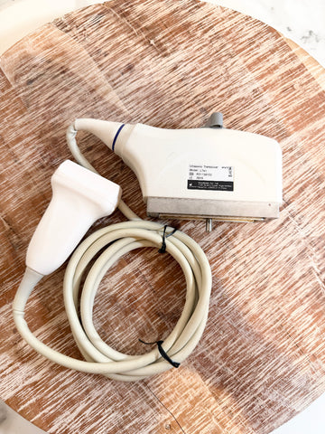 Sonoscape ultrasound machine probe with a coiled beige cable, resting on a round wooden cutting board.
