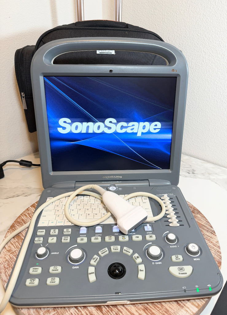A SonoScape portable ultrasound machine with its screen on and attached probe, sitting on a wooden surface with a black carrying case behind it.