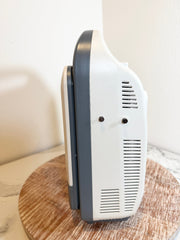 A Sonoscape ultrasound machine shown from a side angle, resting on a round wooden board against a plain off-white background.