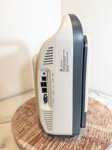 A close-up side view of the Sonoscape ultrasound machine showing its rear and side ports, set on a round wooden surface against a plain white wall.