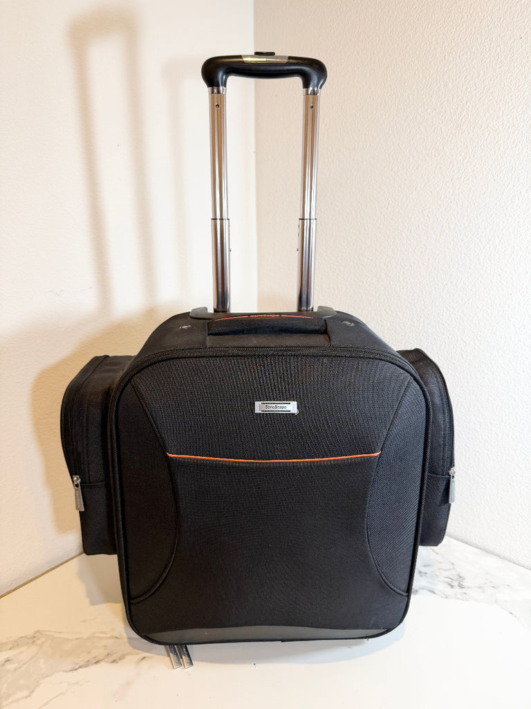 Sonoscape rolling bag with an extended handle, standing upright on a light marble-like surface against a textured off-white wall. The bag features a front zippered pocket with a thin orange accent line and a small silver brand plaque.