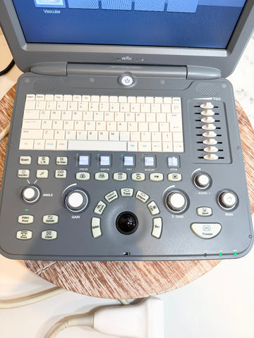 A Sonoscape ultrasound machine with a gray control console, cream-colored keyboard, and trackpad, shown sitting on a wooden surface with its monitor open.