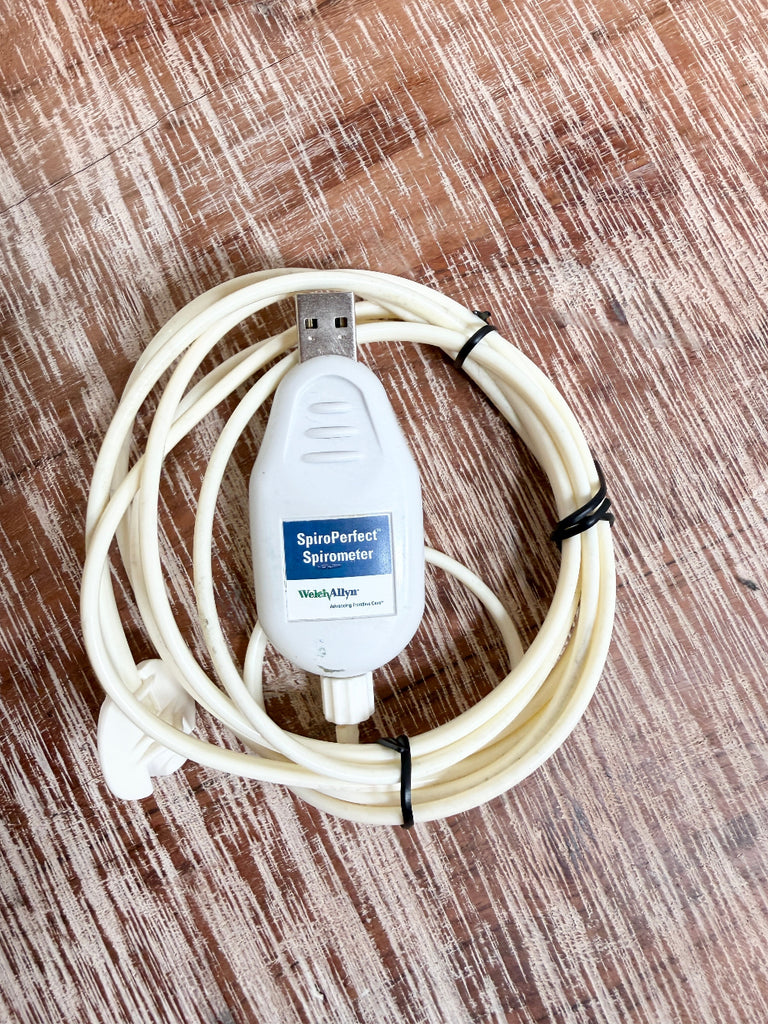 A Welch Allyn SpiroPerfect 703554 USB Spirometer Sensor coiled white USB spirometer cable with a central white control module labeled 'SpiroPerfect Spirometer' and 'Wash & Filter,' photographed on a brown wood-grain surface.