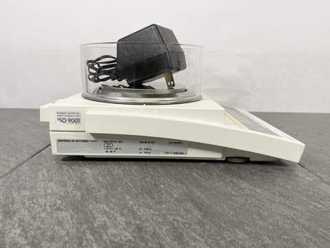 Side picture for Sartorius AG Gottingen BP110-0U2 Laboratory Balance Scale with an power adapter placed on top of the unit